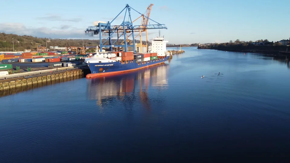 A large container vessel alongside port cranes, illustrating international freight coordination